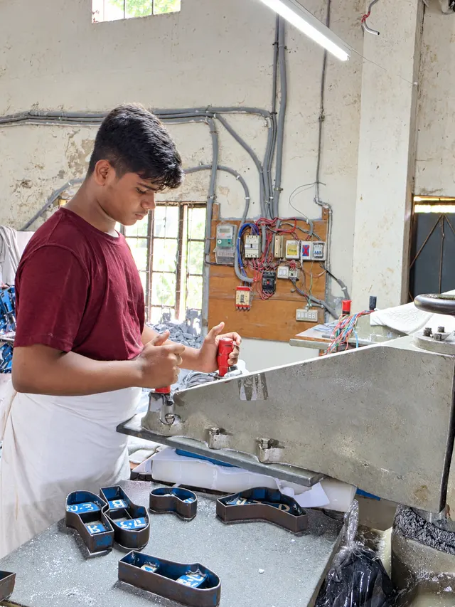 Team member in a burgundy shirt and white apron at a leather cutting press