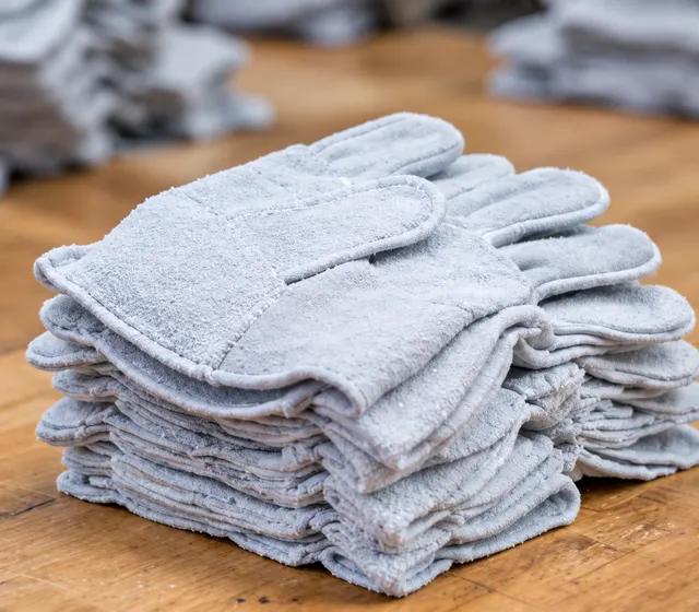 Stacked pale split leather gloves with sewn seams and short cuffs on a wooden worktable