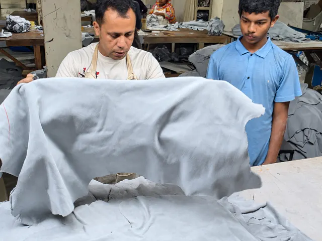 Two workshop team members handling a large pale leather sheet at a worktable